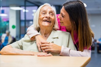 Happy elder woman and nurse embraced in a nursing home