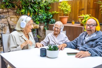 Happy elder people enjoying music with headphones in the garden of a nursing home