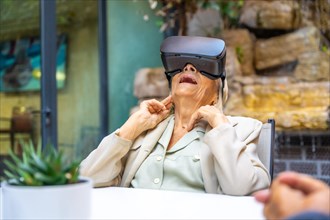 Elder woman looking up while using Virtual reality goggles sitting on a geriatric