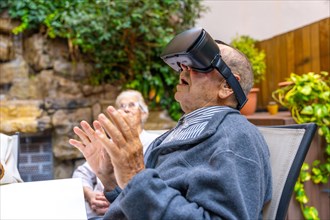 Elder man using virtual reality goggles sitting on the garden of a geriatric