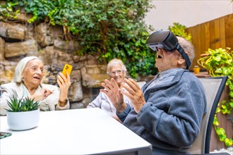 Elder man using virtual reality goggles sitting on the garden of a nursing home