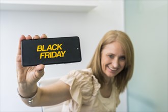 Beautiful mid-adult woman showing a smartphone with Black Friday advertisement on the screen
