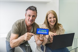 A man holds his smartphone with Cyber Monday advertisement on the screen with her wife on his side