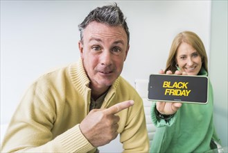 A man shows his smartphone with Cyber Monday advertisement on the screen with her wife on his side