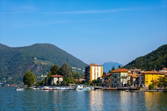 City of Porto Ceresio on Waterfront with Mountain and Lake Lugano in a Sunny Summer Day in Porto Ceresio