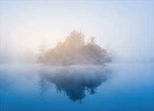 Foggy sunrise at a lake. Island and trees in blue and orange light