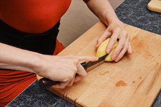 Unrecognizable woman slicing peeled potato on cutting board