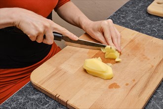 Female hands cut potatoes on wooden cutting board. Making potato casserole