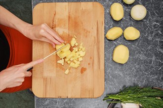 Preparation of soup or dinner in the kitchen. Woman cutting potatoes on wooden board