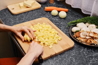 Unrecognizable woman chopping chopped potatoes with a knife on cutting board