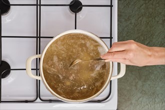 Top view of unrecognizable woman mixing soup in a casserole on a gas stove