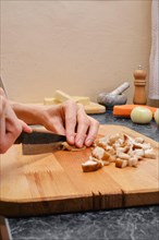 Unrecognizable woman slicing shiitake mushroom on wooden cutting board