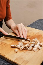 Close up view of female hands cutting shiitake on wooden cutting board