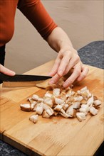 Female hands with knife cutting shiitake mushroom on wooden cutting board