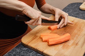Close up view of hands of woman cutting carrot on wooden cutting board