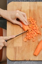 Top view of female hands chopping carrot on wooden cutting board