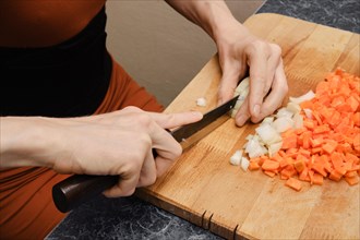 Close up view of hands of unrecognizable woman slicing onion on wooden cutting board