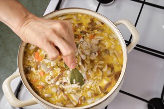 Top view of hand of woman adding bay leaf to soup on a gas stove