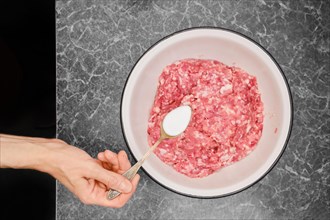 Hand of woman adding salt on spoon to minced meat