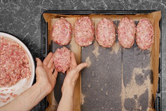 Unrecognizable woman put beef meat patties on baking tray