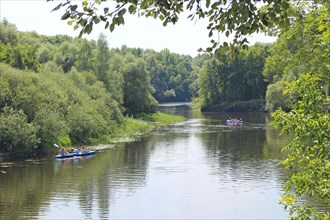 Group of people are sailing on kayaks along a beautiful river. Summer holidays. Sports and recreation on the river in summer. Kayaking on the river. Friends spending time together sailing in river