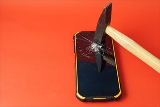 Hammer breaking the screen of a mobile phone on a red background