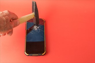 Man's hand with a hammer smashing a mobile phone screen on a red background