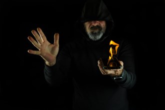 Hooded man dressed in black holding a flaming cell phone on a black background