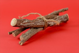 Pile of licorice roots tied with a rope isolated on red background
