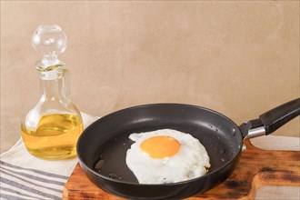 Fried egg with extra virgin olive oil in a frying pan with a glass bottle with oil on a wooden board