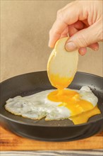 Woman hand Dipping bread on the yolk of an egg fried in olive oil with a frying pan on a wooden board