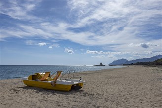Yellow pedal boat on the beach in front of the Torre Di Bari Sardo tower in the distance