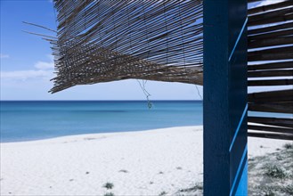 Straw mat hanging in the wind on a hut on a white sandy beach in front of a bright blue sea