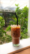 Vertical view of a glass of iced cappuccino perched on a veranda on a hot summer day