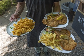 A waiter serves schnitzel and fried calamari in a garden restaurant