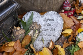 Mementos and stones in the shape of a heart on a memorial tree with the names of the buried