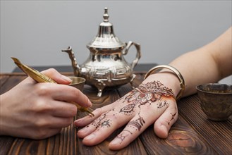 Artist making mehndi womans hand near teapot