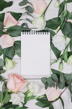 Blank spiral notepad surrounded with pink rose flowers wooden desk