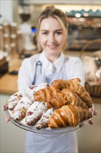 Blurred young woman offering croissants glass cake stand