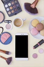 Cellphone screen coffee with macaroons cosmetics products beige background