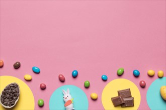 Choco chips rabbit statue chocolate pieces colorful candies pink backdrop with space text