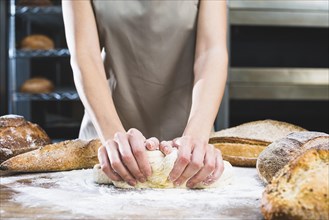 Close up female baker kneading dough with flour wooden surface