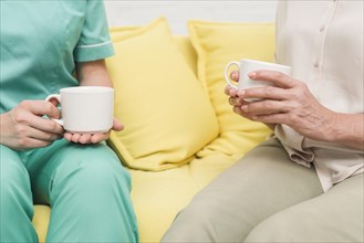 Close up nurse patient sitting sofa holding coffee cups