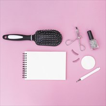 Cuticle hair brush sponge fake eyelashes eyelash curler nail polish bottle with blank spiral notepad pink backdrop