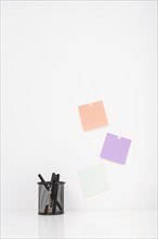 Different pens holder near colorful adhesive notes stucked wall