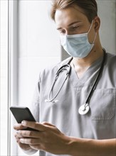 Doctor with medical mask checking smartphone