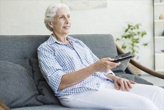 Elderly woman watching television using remote