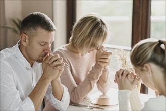 Family praying together before eating indoors