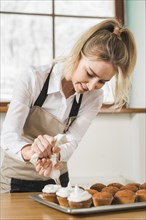 Female baker decorating cupcake with white butter cream by squeezing icing bag