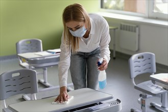 Female teacher disinfecting school benches classroom